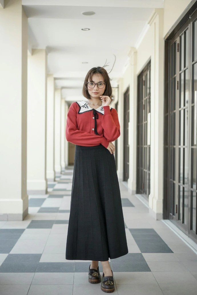 A woman standing in a hallway wearing a red shirt and black skirt
